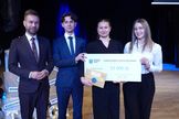 Czwórka osób pozujących do zdjęcia. Trójka osób trzyma dużą kartkę z napisem nagroda.