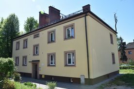 Jasny, piętrowy budynek mieszkalny, zieleń, w tle błękitne niebo. 