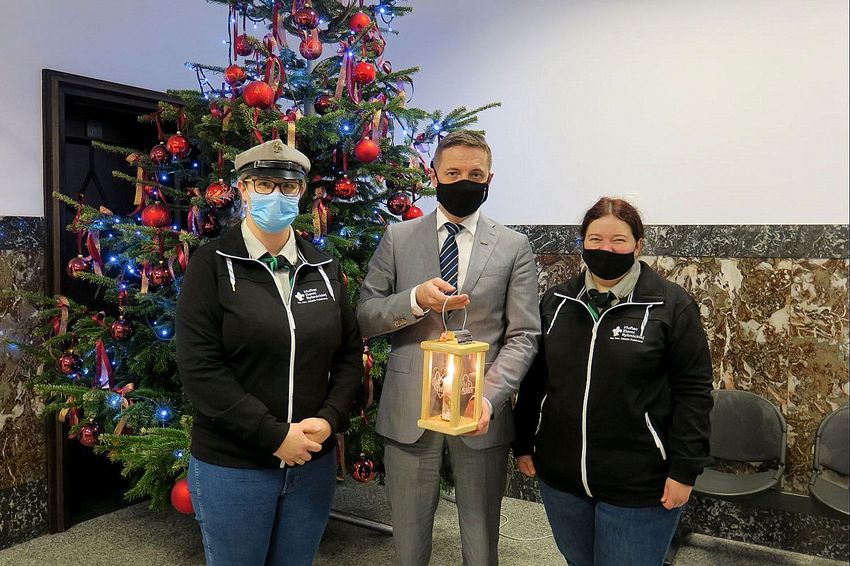 Dwie harcerki z prezydentem Rybnika trzymającym ogień betlejemski. W tle choinka