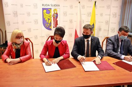Dwie kobiety i dwóch mężczyzna podpisują dokumenty przy wspólnym stole. W tle ścianka promocyjna z logosami. 