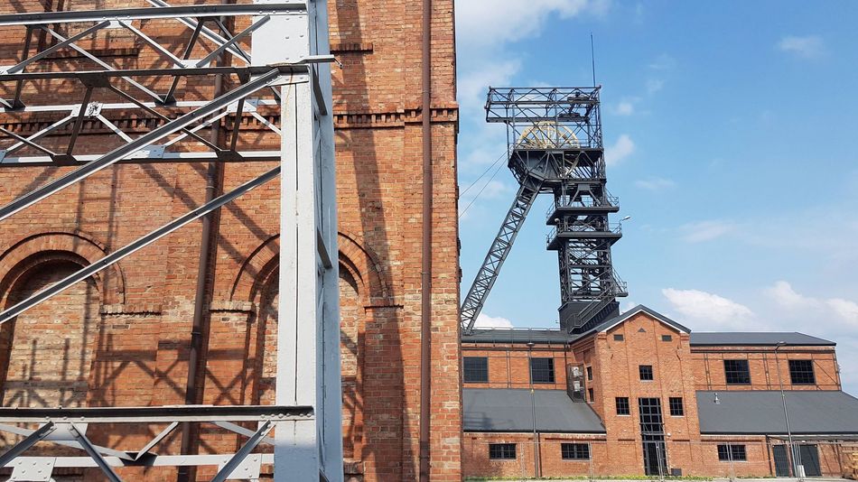 Zabudowania kopalni Ignacy, ceglane budynki, szyb kopalniany na tle błękitnego nieba.