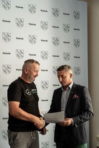 Zdjęcie przedstawia mężczyznę, któremu drugi mężczyzna wręcza dyplom.