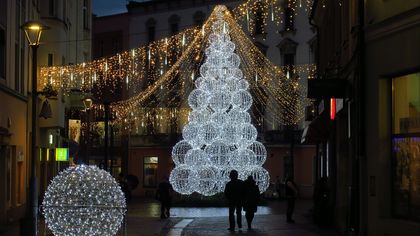 Wieczór. Świątecznie udekorowane miasto - lampki nad ulicami, choinki, i inne ozdoby.