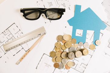 Rozłożone plany architektoniczne domu, na nich leżą czarne okulary, drewniany ołówek i linijka.