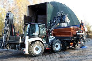 Ulice miasta, na nich pługopiaskarka i pracownicy służb komunalnych z szuflami do odśnieżania.
