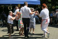 Grupa osób tańćząych w kółku podczas plenerowego festynu