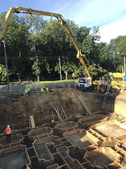 Budowa budynku - widoczne fundamenty oraz fragmenty konstrukcji betonowej i żelaznej. W tle osiedle zieleń. 