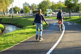 Asfaltowa droga rowerowa wzdłuż rzeki, dziewczyna na rolkach, chłopak na rowerze