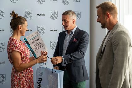 Zdjęcie przedstawia kobietę, która trzyma dyplom i dwóch mężczyzn.