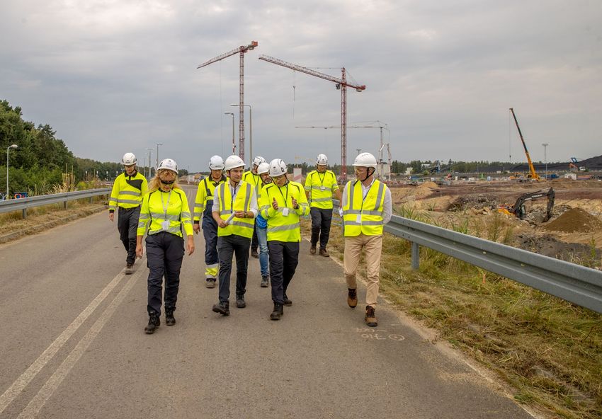 Grupa osób w odblaskowych kamizelkach wiztuje budowę