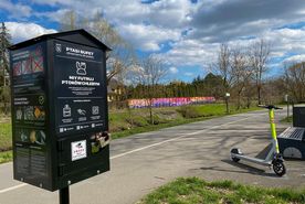 Automat, w którym można kupić karmę do karmienia rzecznego ptactwa., w tle bulwary i stojące hulajnogi
