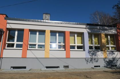 Piętrowy budynek szkoły po remoncie. Wokół niezagospodarowany teren zielony.