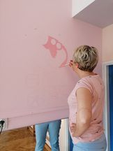 OsrodekJPII remont 9 Kobieta koloruje na różowej ścianie wzór biedronki na rowerze.