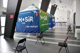 Szeroki korytarz, na którym stoją dwa namioty z napisem MOSiR oraz kilka krzeseł