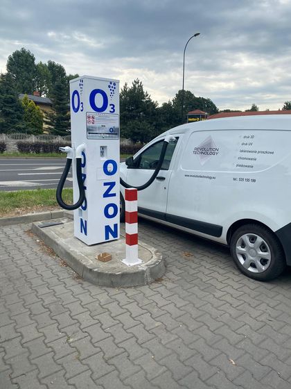 Urządzenie do ozonowania samochodu w trakcie pracy. W tle ulica, zieleń i zachmurzone niebo.