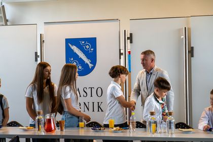 Zdjęcie przedstawia czwórkę dzieci i mężczyznę. Mężczyzna podaje rękę chłopcu. 