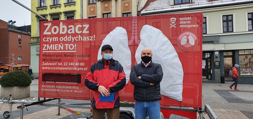 Instalacja przedstawiająca ludzkie płuca, ustawiona wśród zabudowy miejskiej. Na ich tle stoi dwóch mężczyzn.