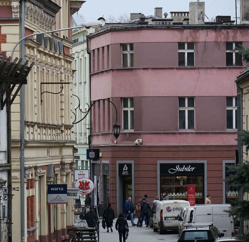 Kamienice w zabudowie śródmiejskiej. Deptak, na nim przechodnie i stojące samochody
