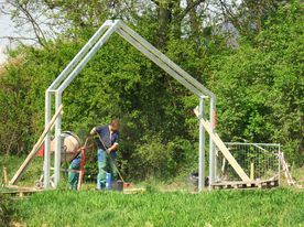 Fragment terenu parku, gdzie dwóch pracowników montuje stalowy trejaż