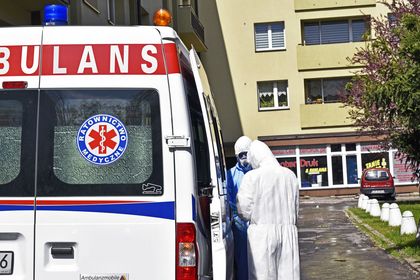 Wymazobus fot.K 4 Karetka pogotowia na podjeździe przed blokiem. Po prawej stronie medycy w kombinezonach ochronnych.