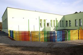 Parterowy budynek, na pierwszym planie kolorowy płot
