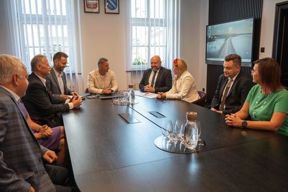 Zdjęcie przedstawia grupę osób siedzących przy stole na oficjalnym spotkaniu.
