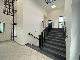 Klatka schodowa, jasne wnętrza, ciemne schody, duże okno z widokiem na zieleń.