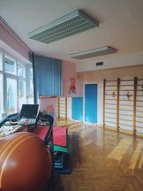OsrodekJPII remont 12 Sala do rehabilitacji - parkiet, drabinki, pomarańczowa duża piłka, urządzenie do ćwiczeń, niebieska żaluzja, na różowej ścianie rysunek - Świnka Pepa