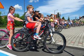 Grupa uczniów na rowerach i hulajnogach na placu szkolnym