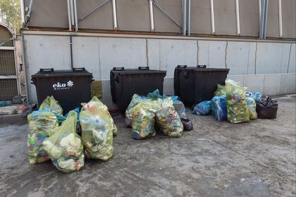 Trzy kontenery na śmieci. Przed nimi leżą żółte worki z posegregowanymi odpadami z tworzyw sztucznych. 