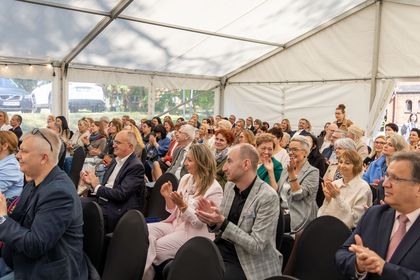 Grupa ludzi siedząca w pomieszczeniu na wydarzeniu oficjalnym. Część ludzi klaszcze w dłonie.