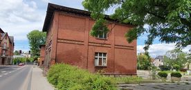 Ceglany budynek przy ulicy, zieleń, błękitne niebo. 