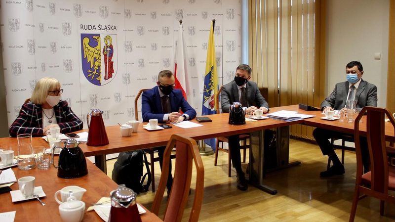 Spotkanie biznesowe: na tle flag i benru z logo miasta Ruda Śląska, za stołem siedzą dwie kobiety i dwóch mężczyzn
