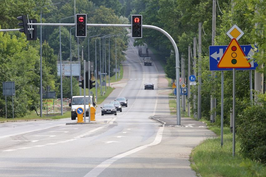 Droga dwukierunkowa otoczona lasem, nad drogą sygnalizacja świetlna