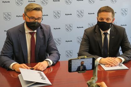 Prezydent Rybnika Piotr Kuczera i wójt Pilchowic Maciej Gogulla podpisują umowę przy stole konferenycyjnym. W tle ścianka reklamowa z herbem Rybnika