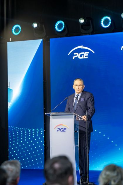 Mężczyzna stojący na scenie, mówiący do mikrofonu.