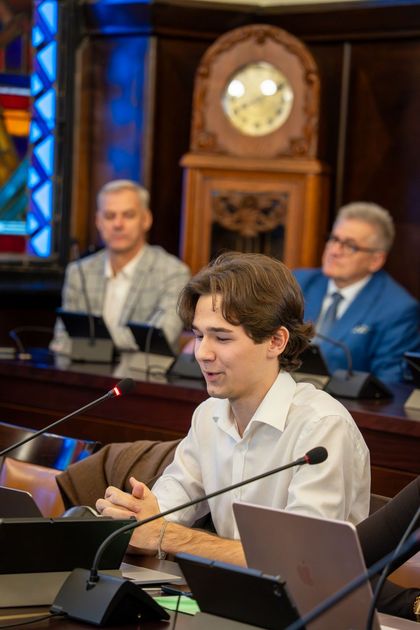 Trójka osób siedząca na sali sesyjnej. 