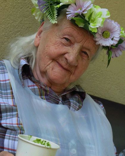 Zdjęcie przedstawia starszą kobietę z wiankiem na głowie.