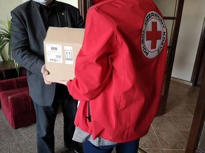 Ratownik medyczny stojący tyłem, odbiera tekturowe pudło od innej osoby