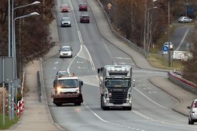Ulice miasta, na nich pługopiaskarka i pracownicy służb komunalnych z szuflami do odśnieżania.
