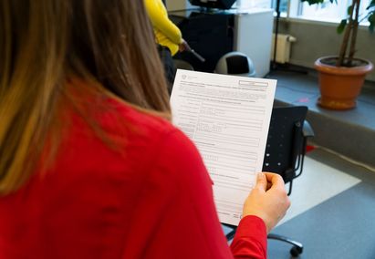 Widziana z tyłu postać kobiety w czerwonym żakiecie z formularzem urzędowym w ręku