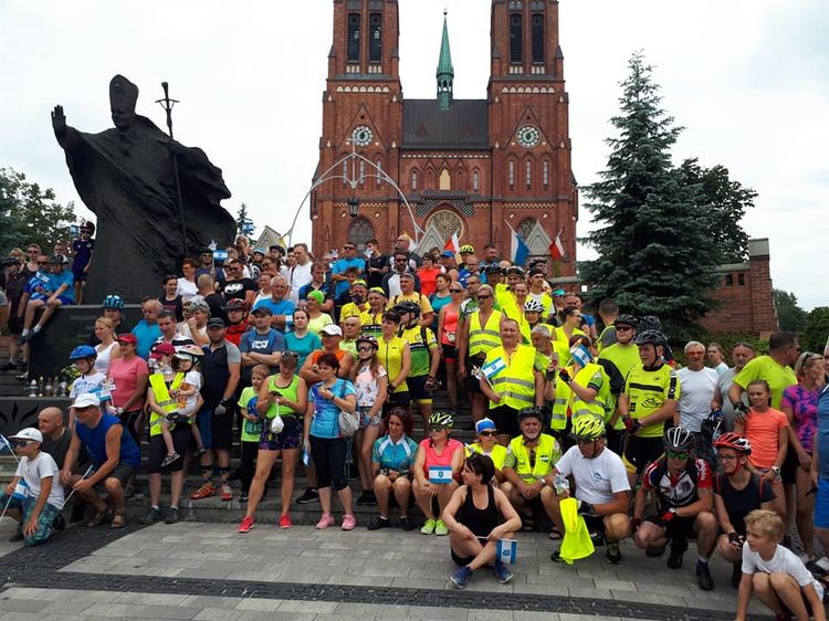 Grupa osób w strojach rowerowych stojąca na schodach przed bazyliką
