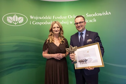 Mężczyzna i kobieta pozują do zdjęcia. Mężczyzna trzyma w rękach nagrodę.