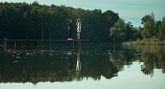 Kadr z filmu Rzeczy niezbędne - dwie osoby na drewnianym pomoście na jeziorze