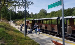 Kolejka wąskotorowa z turystami, stojąca na leśnej stacji