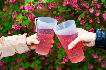 Dwa ekokubki w kolorowym napojem trzymane w dłoniach. W tle zieleń i kwiaty