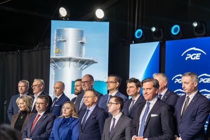 Grupa osób stojących na scenie w sali.