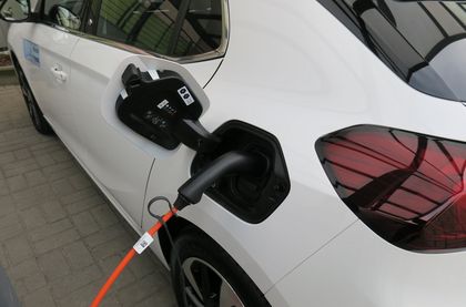 Bok białego samochodu elektrycznego, podłączonego do ładowarki
