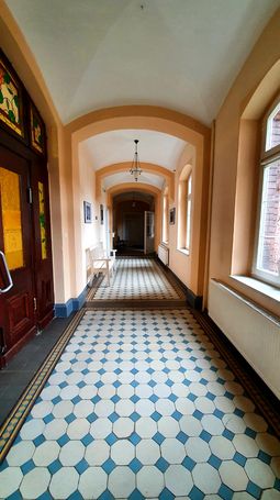 Wnętrze szpitala psychiatrycznego - korytarz z oknami i posadzką z kolorowych płytek 