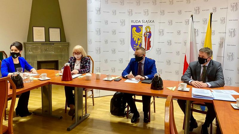 Spotkanie biznesowe: na tle flag i benru z logo miasta Ruda Śląska, za stołem siedzą dwie kobiety i dwóch mężczyzn